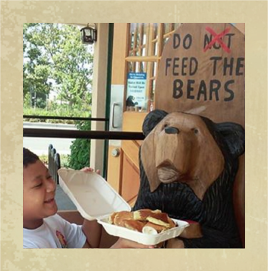 Kid offering food to a Black Bear Diner Wooden Bear